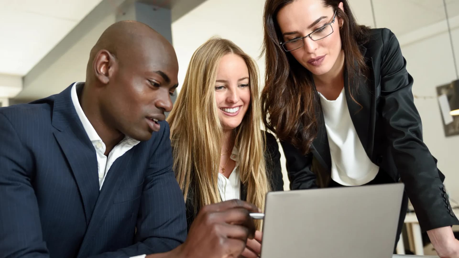 Three business professionals reviewing a website project together on a laptop in a modern office