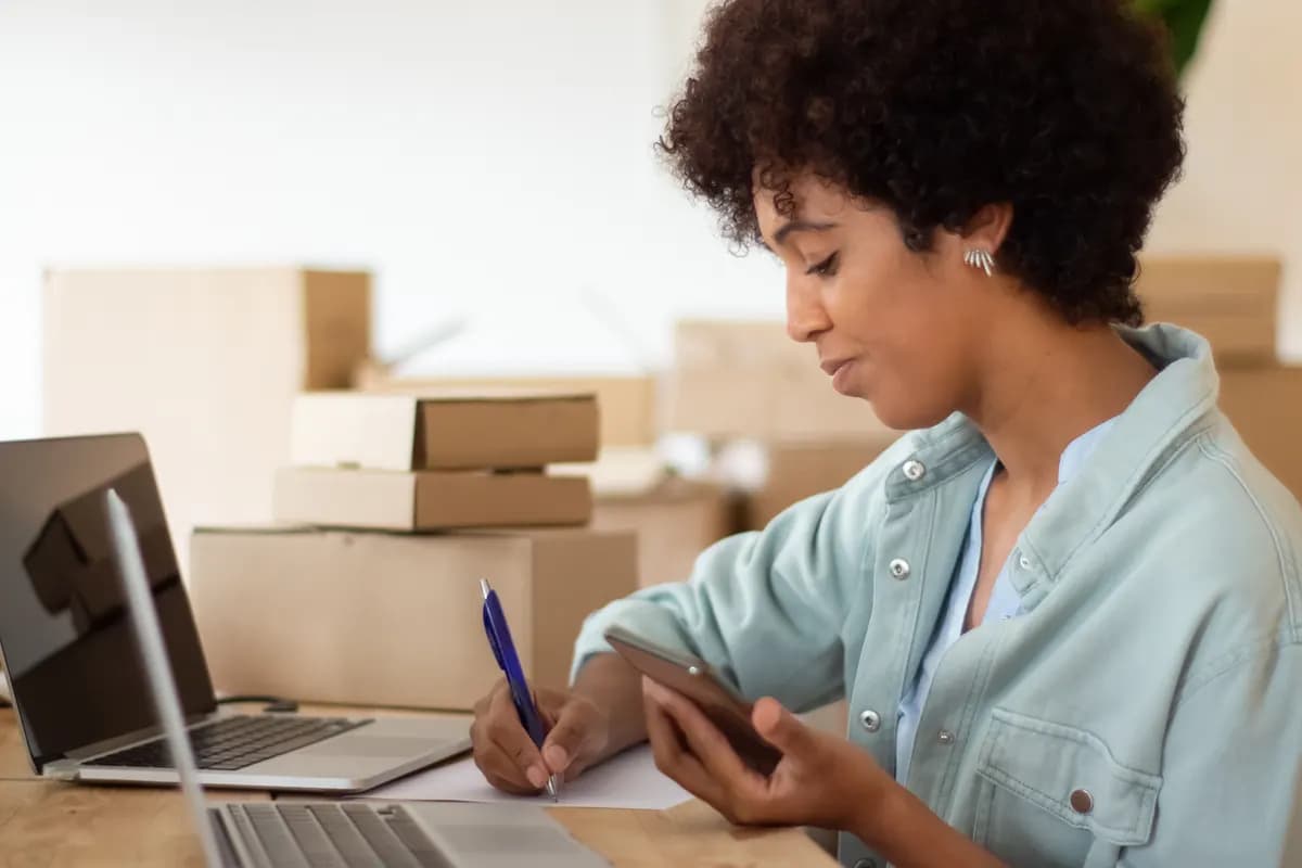An online store owner managing orders on a laptop beside packed shipping boxes